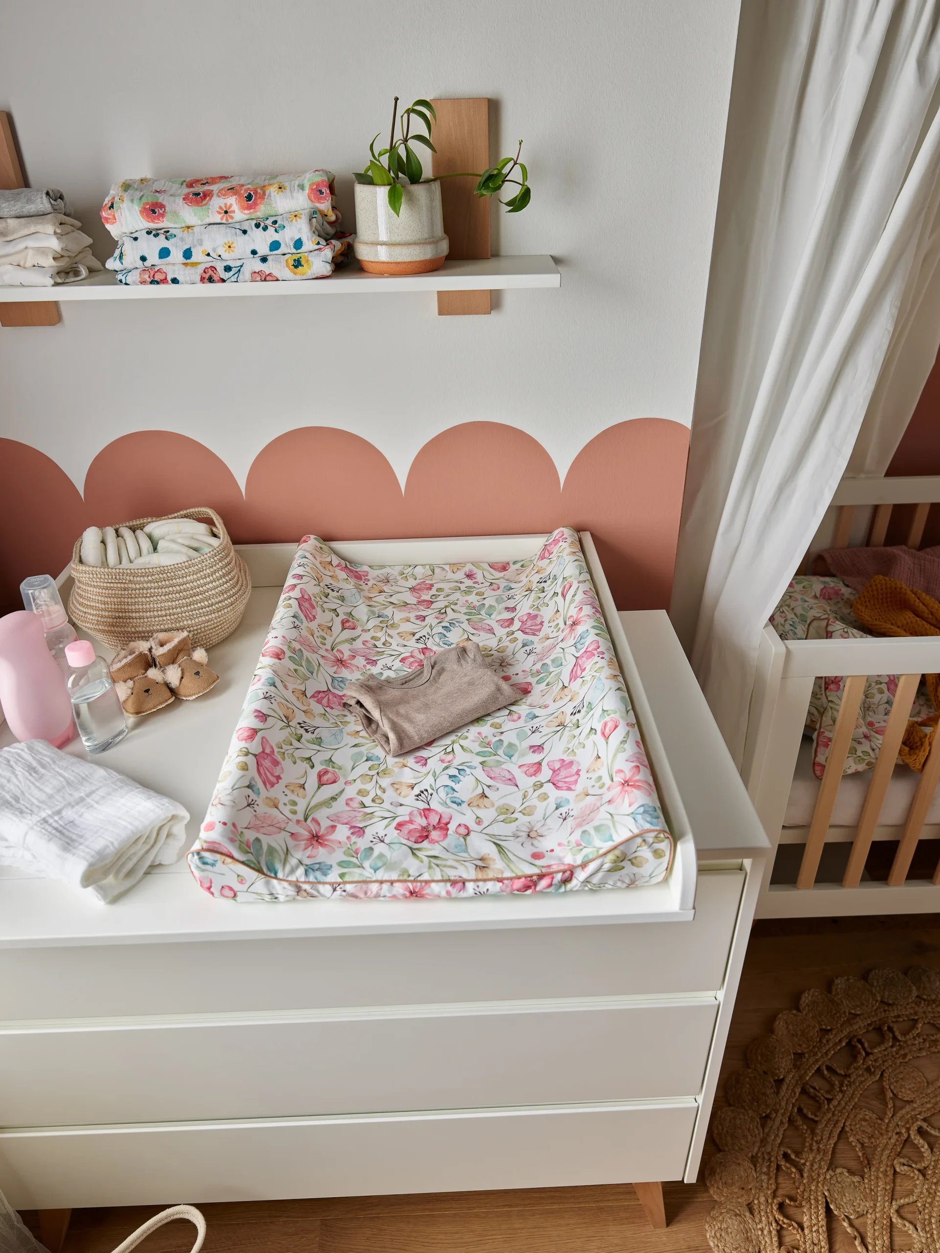 Lifestyle'owe zdjęcie białej komody z szufladami marki Pinio z kolekcji Floral, na blacie znajduje się przewijak pokryty tekstylną matą w kwiatowy wzór, mebel w kolorze białym, standardowy rozmiar, aranżacja w pokoju niemowlęcym
